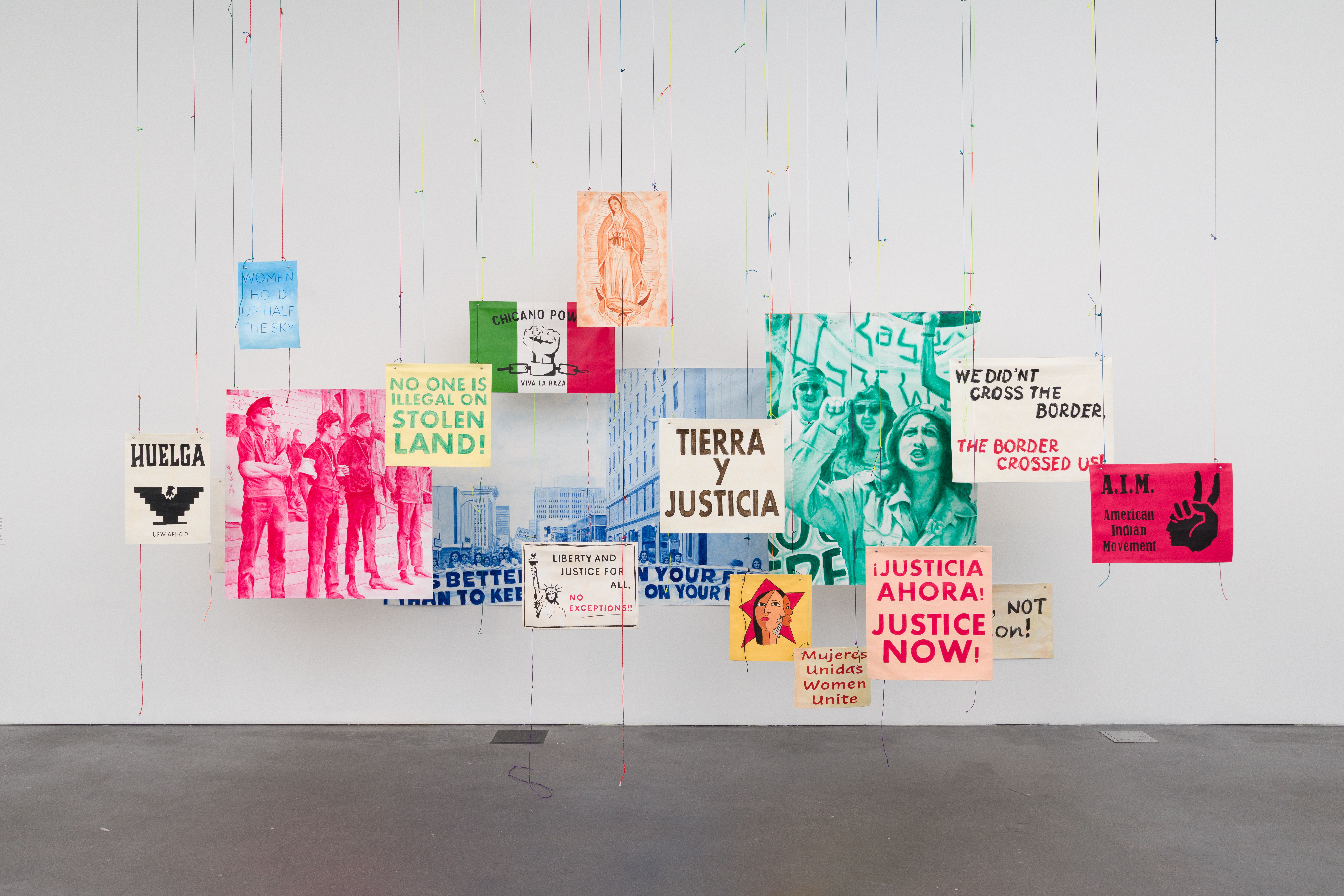 Installation by Carlos Frésquez in Colorado Currents at MCA Denver, hanging painted protest banners including the UFW eagle, Chicano Power, Tierra y Justicia, and American Indian Movement